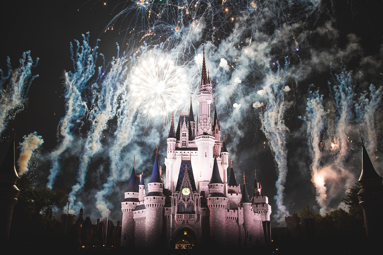 A magical nighttime scene at Disneyland with a blackish sky illuminated by vibrant fireworks bursting in the air. The colorful explosions create dazzling patterns above the iconic castle, which is softly lit, enhancing the enchanting atmosphere of the park.